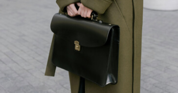 Eine elegante Damen-Businesstasche in Schwarz, gehalten von einer Person in einem olivgrünen Mantel.