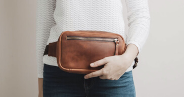 Eine braune Damen Gürteltasche aus Leder, getragen über Jeans und Pullover.