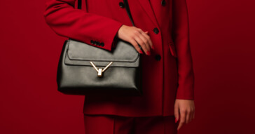 Eine edle Damen-Umhängetasche in Schwarz mit goldenen Details, passend zu einem roten Anzug.