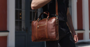 Eine stilvolle braune Herren Businesstasche aus Leder, getragen von einer Person vor einem elegantin Gebäude.