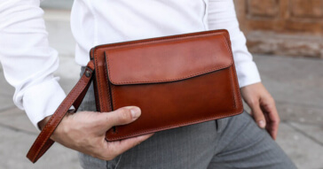 Eine elegante braune Herren-Handgelenktasche aus Leder wird in der Hand gehalten.