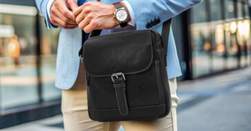Ein Mann mit einer klassischen schwarzen Herren-Handtasche aus Leder in einem geschäftlichen Umfeld.