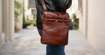 Eine braune Herren-Schultertasche aus Leder wird über der Schulter getragen, passend zu einer Lederjacke.
