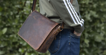 Eine Person trägt eine rustikale braune Unisex-Umhängetasche aus Leder mit verstellbarem Gurt.